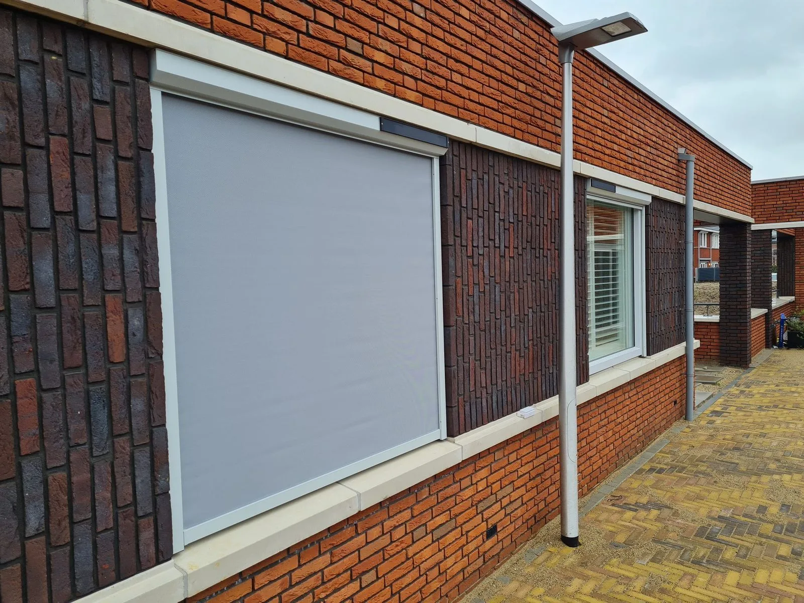 Lichtgrijs screendoek omlaag voor een raam in een rode bakstenen gevel