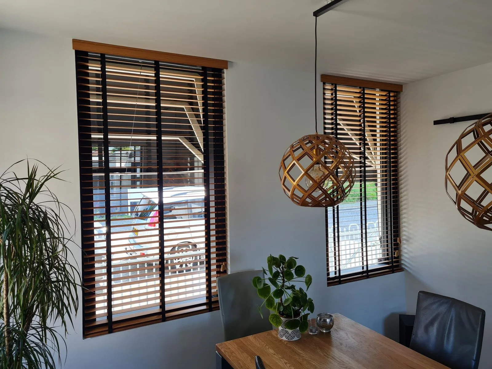 Houten jaloezieën voor twee ramen in een eetkamer met hanglampen