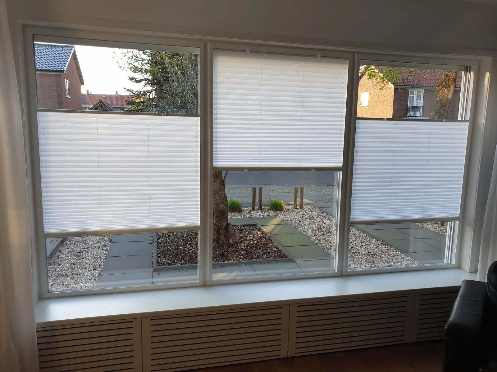 Witte plissés in een frame op drie ramen, half dicht, met uitzicht op een patio