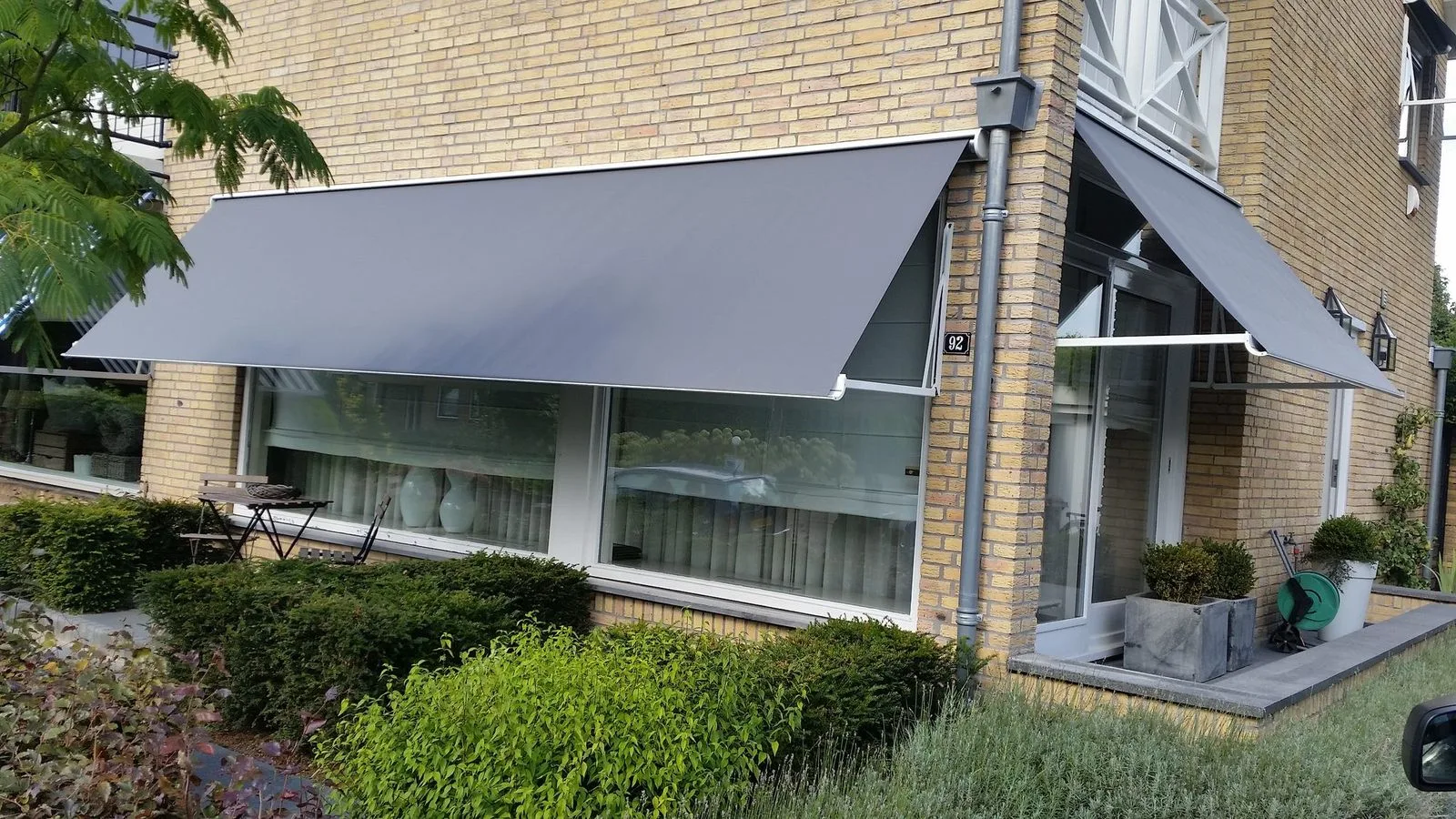 Grijze uitvalschermen boven de ramen op de hoek van een gele bakstenen woning