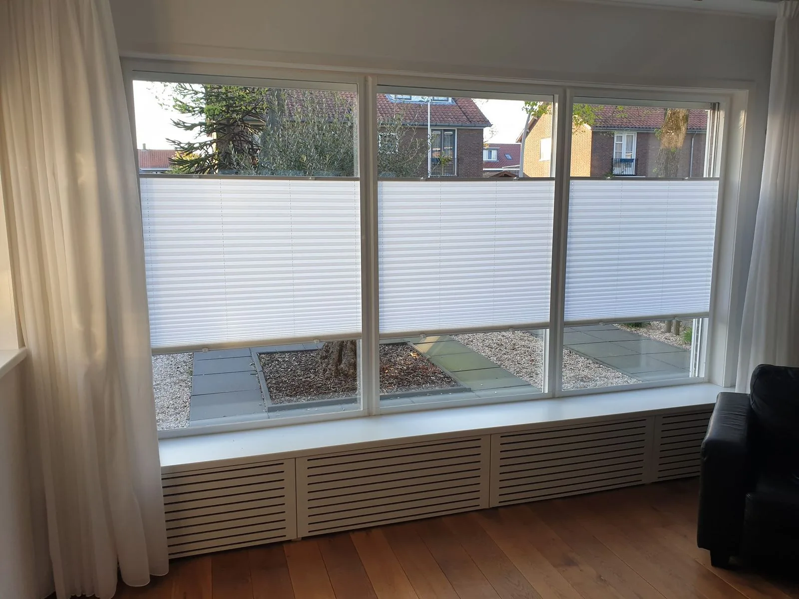 Witte plissés half dicht voor drie ramen, met uitzicht op een patio