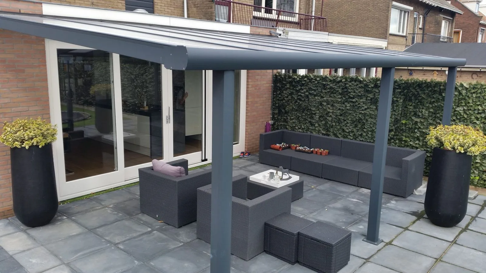 Antracietgrijze terrasoverkapping met loungeset en plantenbakken