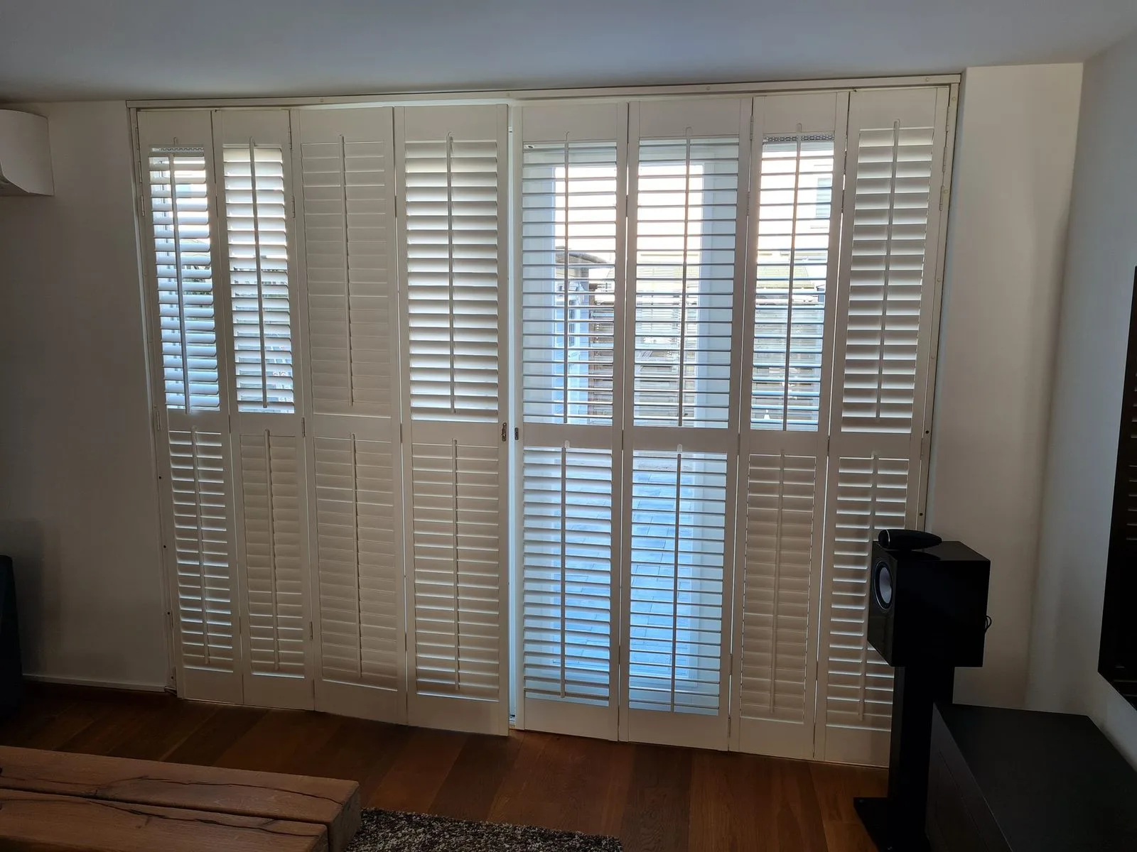 Witte shutters voor een hoge raampartij, deels geopend