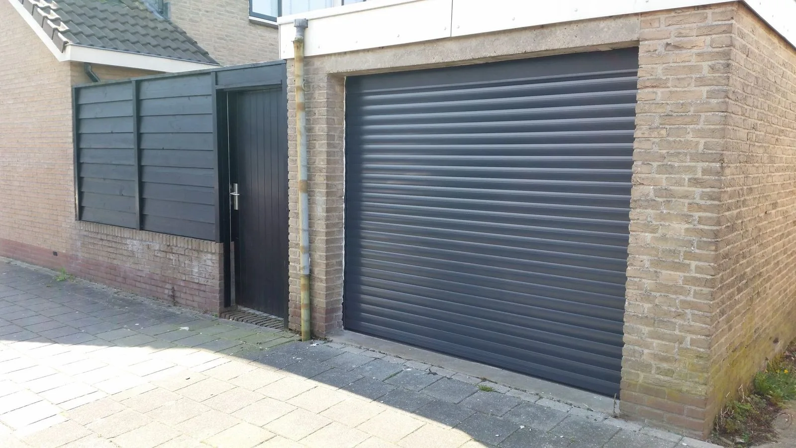 Antracietgrijze rolpoort in een garage van gele baksteen