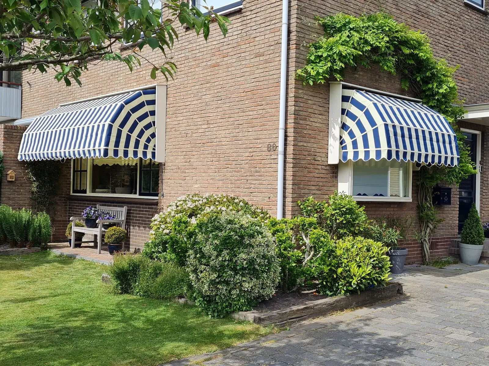 Twee markiezen met blauw-wit gestreept doek boven de ramen van een bakstenen woning