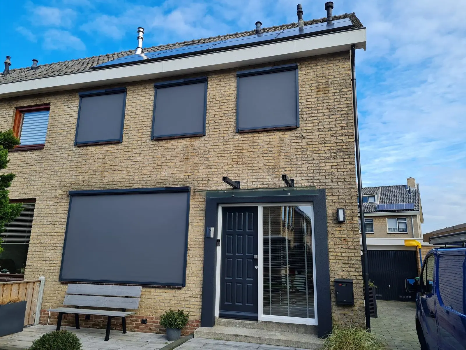 Grijze zipscreens voor de ramen en de pui van een gele bakstenen woning