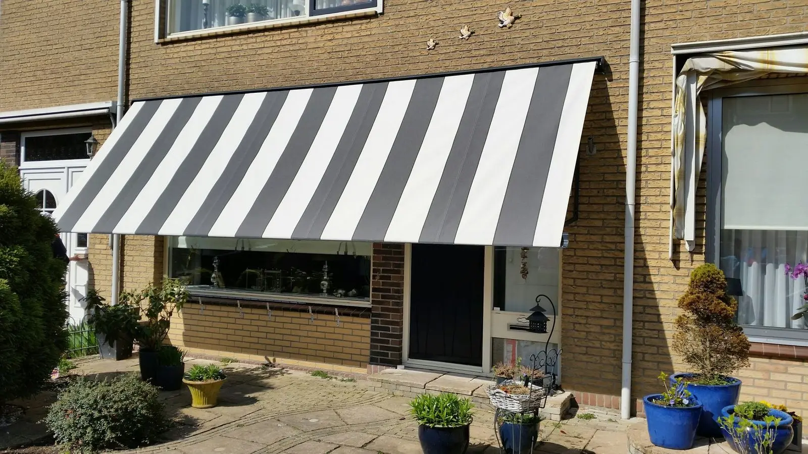 Uitvalscherm met zwart-wit gestreept doek boven een raam naast de voordeur