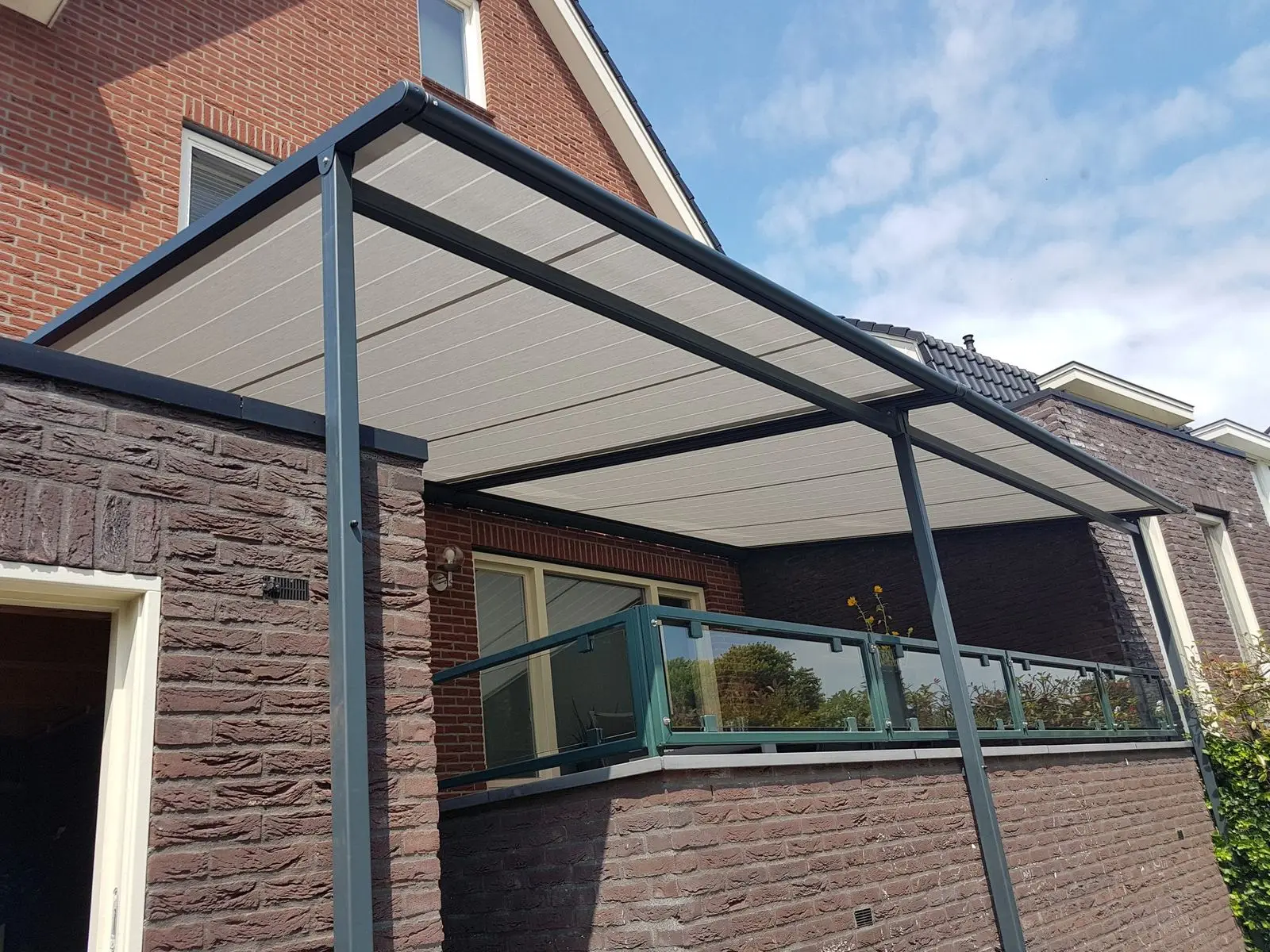 Antracietgrijze pergolazonwering op palen naast een balkon met glazen balustrade