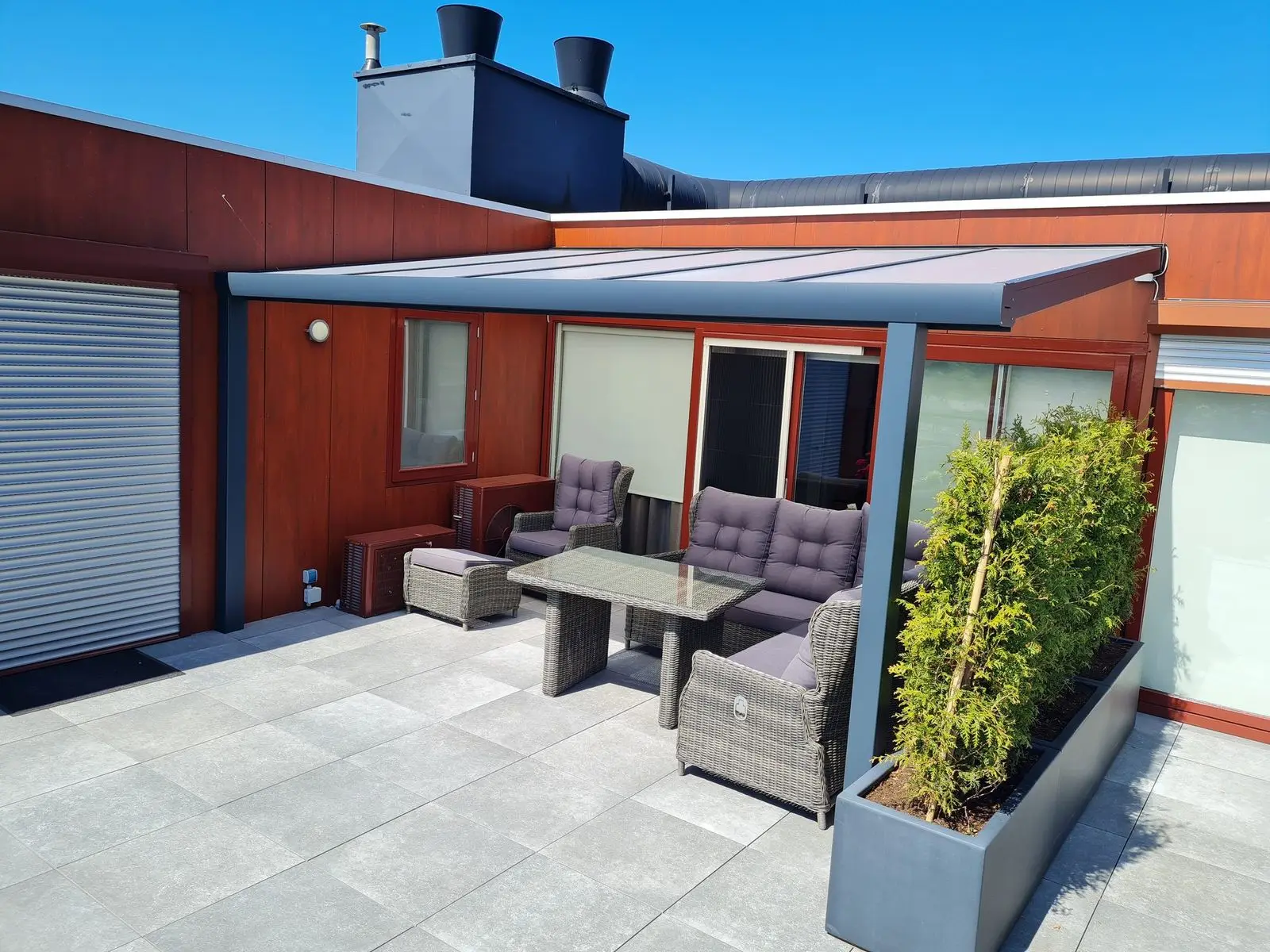 Overkapping met loungeset op een terras naast een aanbouw met rolluik