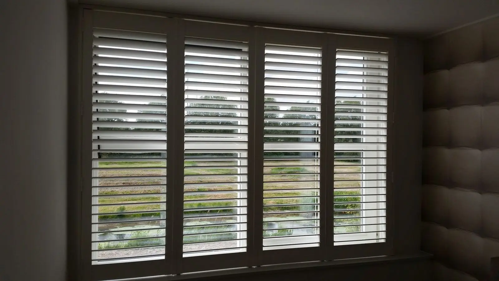 Witte shutters met gekantelde lamellen voor een breed raam