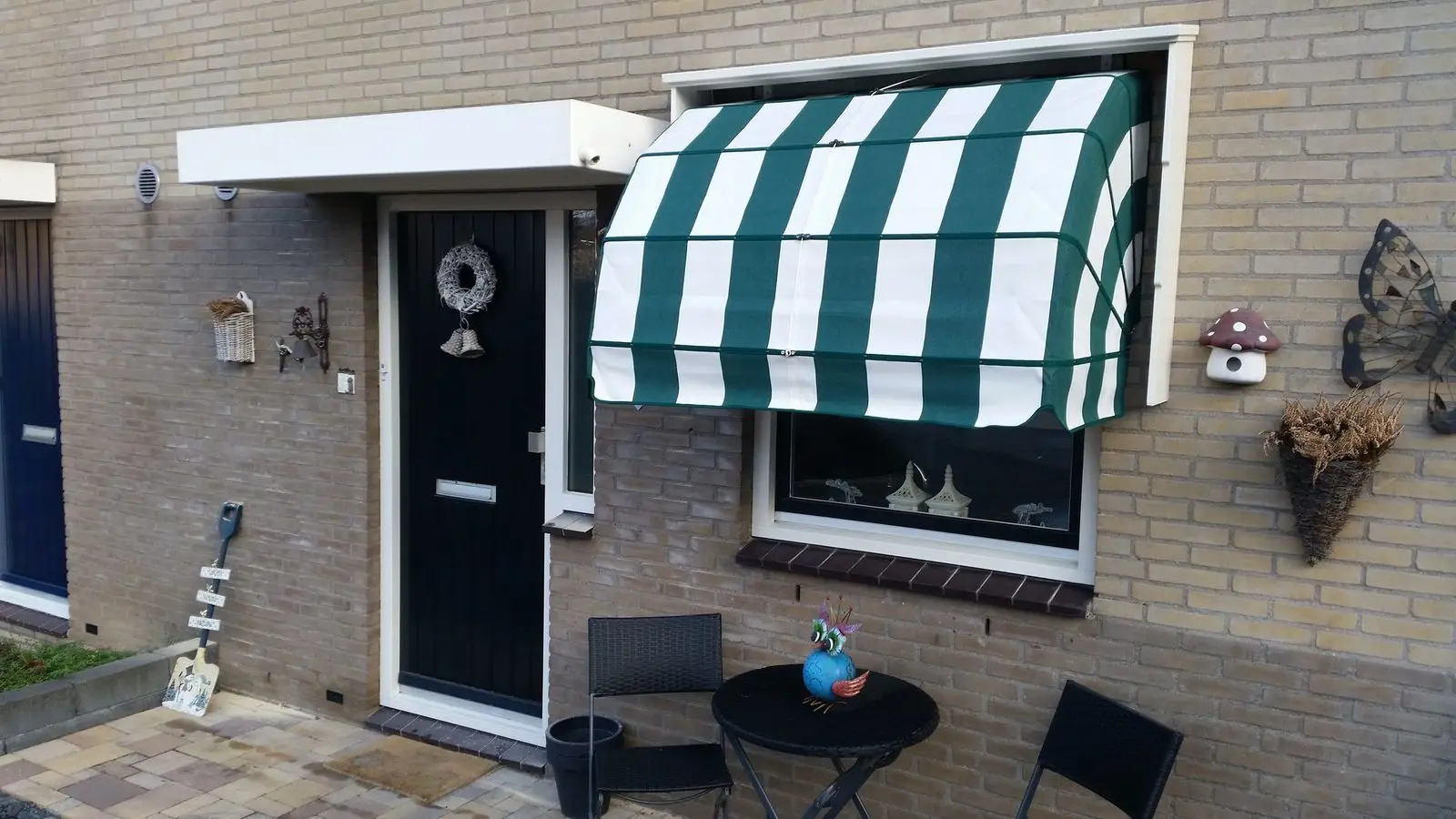 Markies met groen-wit gestreept doek boven een raam naast de voordeur