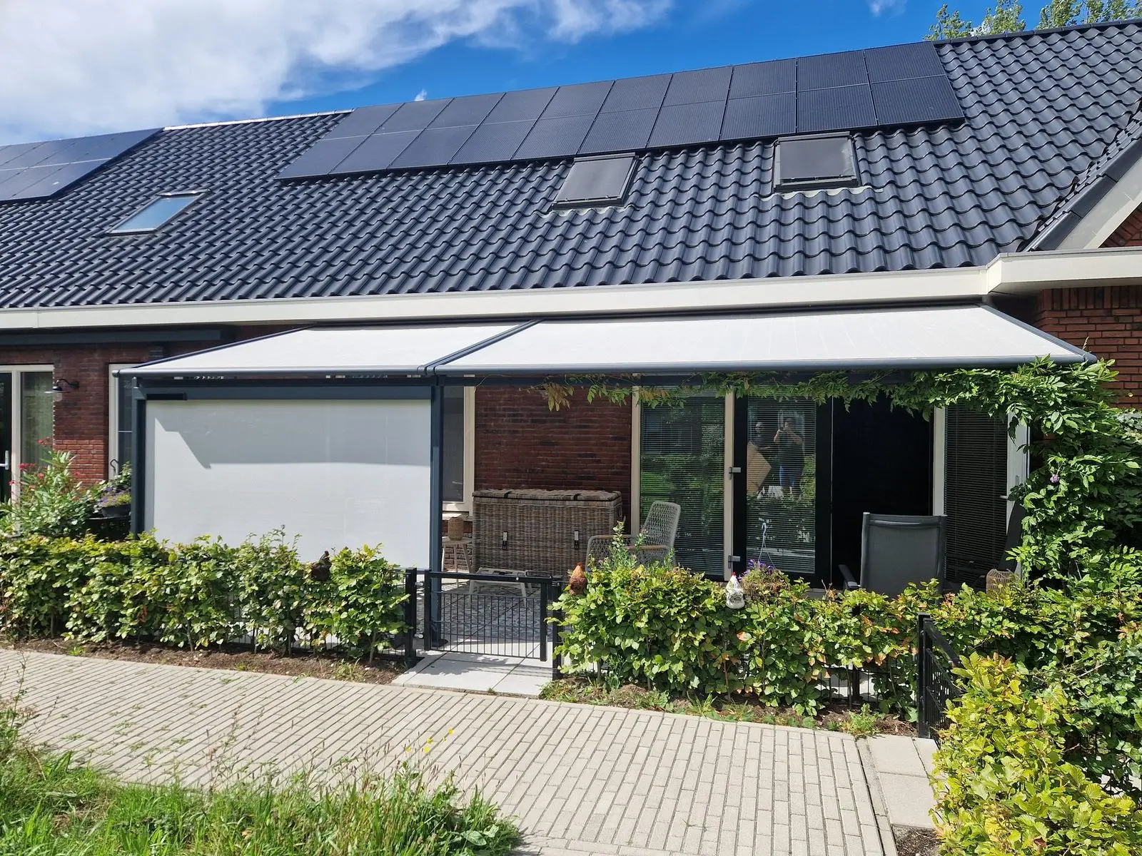 Pergolazonwering met zijscreen aan de achtergevel van een woning met zonnepanelen