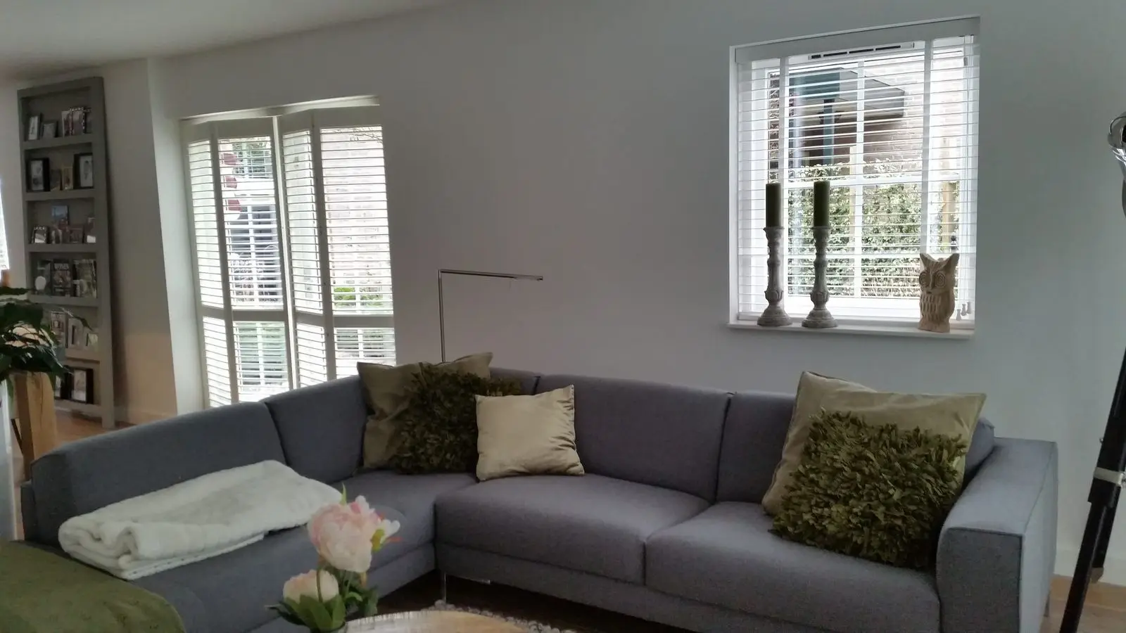 Witte shutters in de ramen van een woonkamer met grijze bank