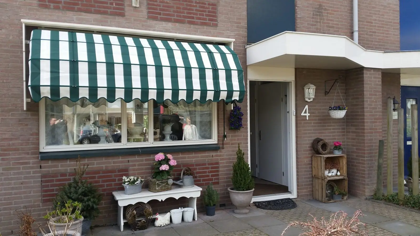 Brede markies met groen-wit gestreept doek boven het raam van een woning