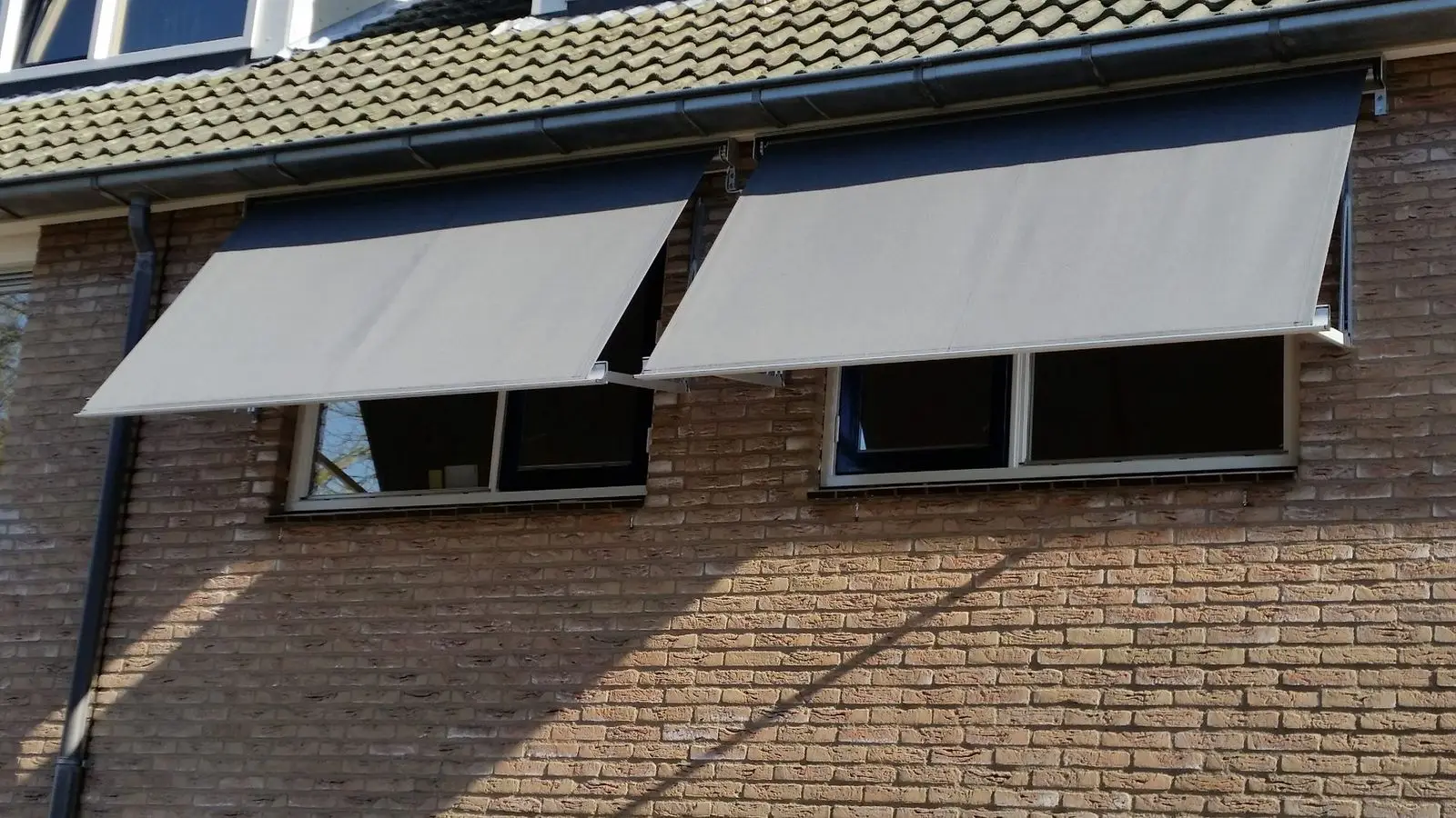 Twee grijze uitvalschermen boven ramen in een bakstenen gevel