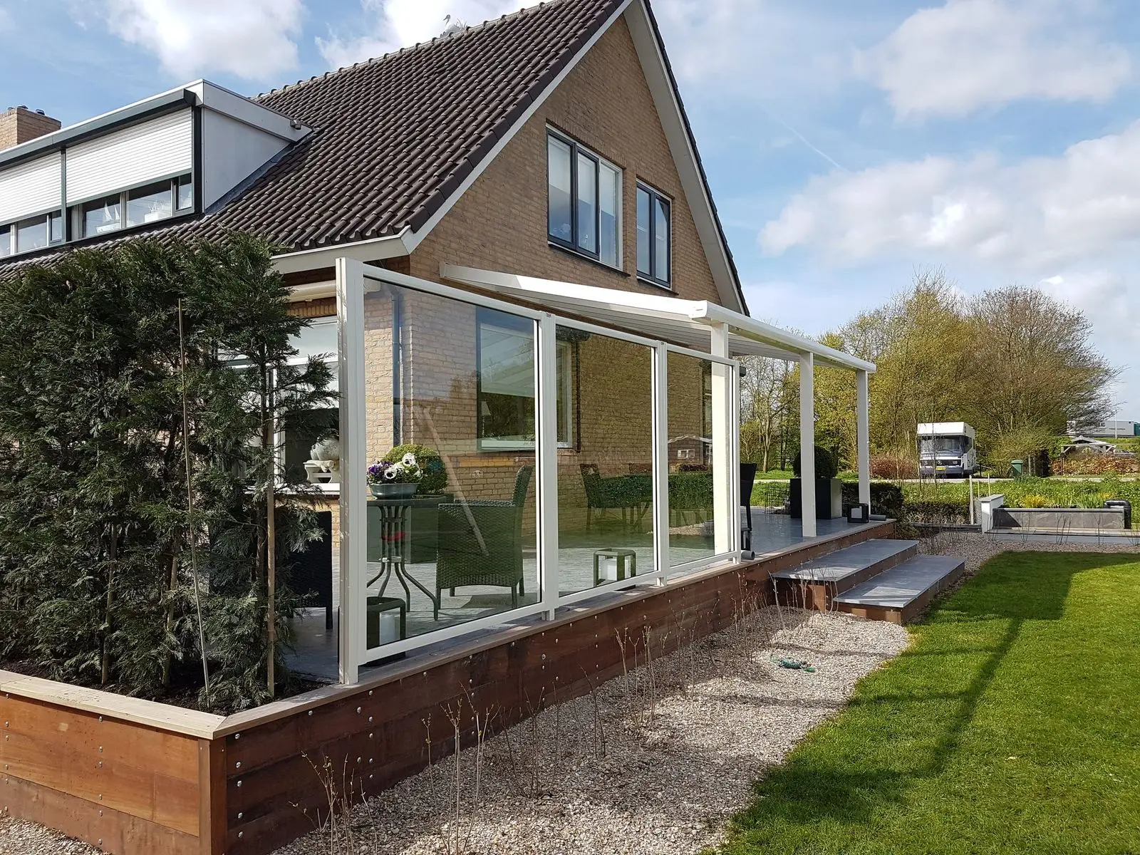 Overkapping met glazen wanden aan een woning, met een houten vlonder