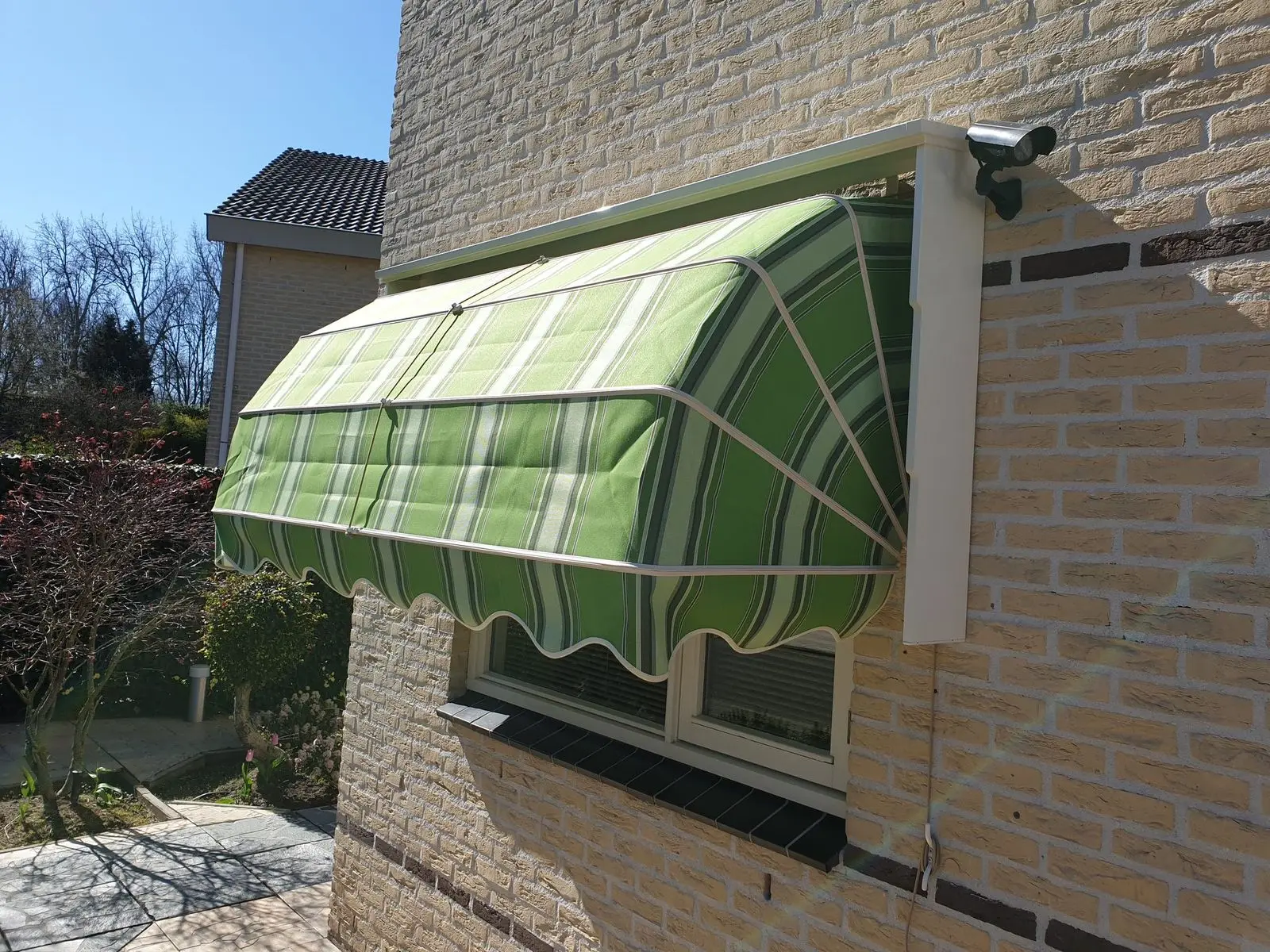 Groene markies met geschulpte rand boven een raam, van opzij gezien