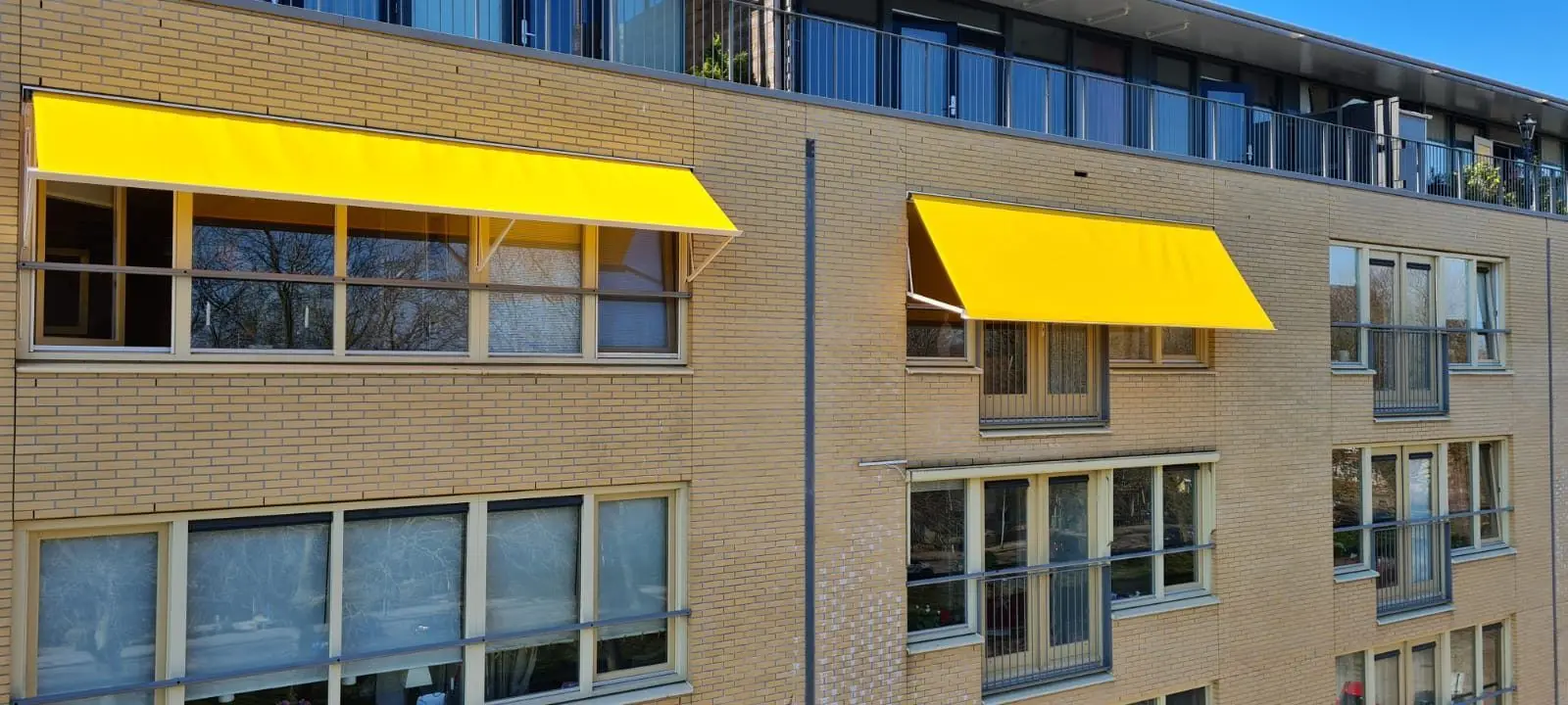 Gele uitvalschermen boven ramen van een appartementengebouw