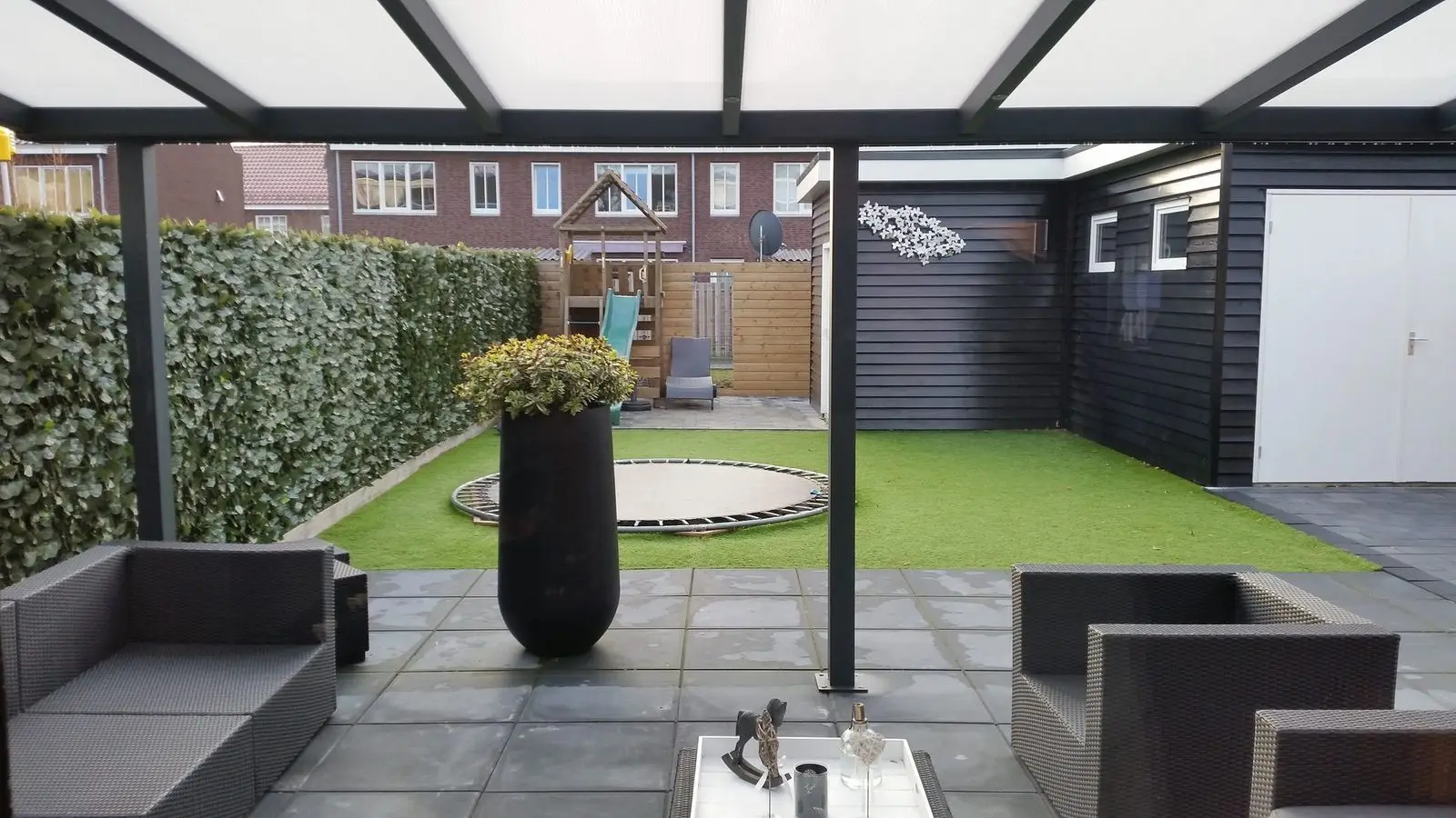 Onder een overkapping gezien: loungeset en kunstgras in de tuin